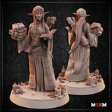 Moon Elf Librarian Cleric by Mia Kay M3DM — standing figure holding an open book, with a scroll in one hand and a stack of tomes cradled at her side, wearing ornately detailed robes with floral scrollwork, long straight hair and a delicate tiara, base scattered with candles and crystal formations.