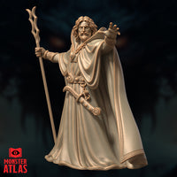 Three-quarter view of a male archmage miniature gripping a branch-like forked staff, extending his right hand forward with fingers splayed, wearing layered robes with a sweeping cloak — 32mm resin by Monster Atlas
