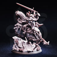 Rear three-quarter view photograph of unpainted Jeanne du Lac mounted paladin miniature — grey resin showing reverse of plate armour, flowing cloak, broken weapons on scenic base, great sword aloft