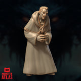 Robed male figure standing upright, cradling a small skull totem in both hands, wearing a heavy cowl and rope belt with bone bead necklace. Grim, bearded expression. Sculpt by Monster Atlas.