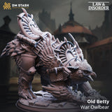 Digital render of Old Betty the War Owlbear miniature from DM Stash Law and Disorder collection, shown in unpainted grey resin colour, crouching low with beak forward, wearing a full spiked war harness with a sweeping ceremonial blade crest rising from her back, taloned feet resting on shattered cobblestone base, city buildings visible in background