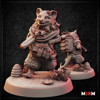 Unpainted grey resin renders of the Opossumfolk Herbalist miniature — front view shows a stout opossum-folk figure mid-stride, wearing a roughspun scarf filled with tiny joeys, pine cones and herb bundles at her belt, a wide toothy grin, and textured fur detail throughout; a small beehive skep sits at the base among foliage. Rear view shows a second pose of the same character from behind, laden travelling pack on her back and staff in hand. M3DM logo visible.