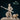 Digital render of Xira the Orc Monk miniature — unpainted cream resin, holding a long diagonal bone staff in a wide combat stance, wearing Celtic knotwork robes with a sash and bracers, with a detailed shaggy bear companion beside her. Front view.