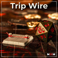 Painted grey resin trip wire trap terrain piece on a battle map grid, showing a wooden plank base with two posts and a red thread strung between them, photographed next to a D&D d20 die