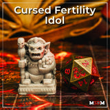 Photograph of the printed Cursed Fertility Idol miniature in unpainted grey resin, shown beside a large gold D20 dice for scale — detail visible includes the skull staff, soul-face necklace, textured skin, and carved decorative base