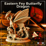 Photograph of the printed Eastern Fey Butterfly Dragon miniature, unpainted grey resin, shown on a tabletop gaming map alongside a D20 die for scale. The sculpt shows clear detail across the butterfly wings, scaled body, and naturalistic root base.