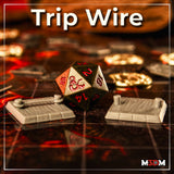 Two painted grey resin trip wire trap terrain pieces on a battle map grid — one with a rope between posts, one with bare posts — photographed either side of a D&D d20 die