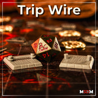 Two painted grey resin trip wire trap terrain pieces on a battle map grid — one with a rope between posts, one with bare posts — photographed either side of a D&D d20 die