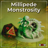Photograph of the printed Millipede Monstrosity miniature painted in pale green and white tones, displayed beside a large black and red D20 dice for scale, showing the segmented body, multiple curved claws, and snarling humanoid upper form in detail