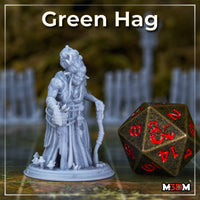 Photograph of a printed and unpainted Grey resin Green Hag miniature at 32mm scale, shown beside a large D20 dice for scale reference — the figure leans forward with a wide grin and clawed fingers, staff in hand and mushrooms at her feet