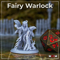 Printed and unpainted grey resin Fairy Warlock miniature by Mia Kay M3DM photographed on a gaming mat beside a large bronze D20 die, showing the full sculpt with moth wings, horns, lantern, chain, and scenic base at 32mm scale