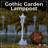 Photograph of the Gothic Garden Lamppost printed miniature in unpainted grey resin, shown on a tabletop gaming mat with multiple lamppost minis visible in the background soft-focus, with a large bronze D20 dice for scale reference