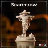 Wicker-bodied scarecrow miniature with pumpkin head and wide straw hat, arms spread on a wooden crossbeam, fraying rope tails hanging at its sides, small pumpkins clustered around the base. Sculpt by Mia Kay M3DM.