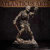 Close-up render of the Atlanticus Arts zombie miniature showing the raised clawing hand, hollow sunken eyes, and decayed armour straps across the chest. The corroded sword is held low at the side. The base is covered in scattered skulls and bones beneath the figure's feet.