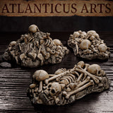 Close view of three Atlanticus Arts bone pile terrain pieces on a dark surface — mounded skull heaps with layered bones and a flat elongated piece showing multiple skeletal forms with visible ribcages and cranial detail.