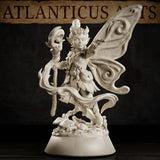 Pixie miniature with large swirling butterfly wings spread wide, wild upswept hair, leaf armour, and a sinuous staff with a grinning mask head, posed over a forest debris base. Sculpt by Atlanticus Arts.