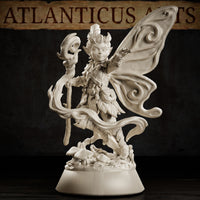 Pixie miniature with large swirling butterfly wings spread wide, wild upswept hair, leaf armour, and a sinuous staff with a grinning mask head, posed over a forest debris base. Sculpt by Atlanticus Arts.