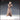 Three-quarter view of an unpainted 32mm resin miniature of a barefoot female beggar in a long patchwork robe with cross-stitch seam detail, rope belt, and long matted hair covering her face, hands pressed together at chest height in a pleading or praying gesture