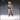 Front-facing digital render of the Hungry Child 01 miniature by Novaminis — an unsettling humanoid figure with wild spiked hair, blank eyes, and arms outstretched in a grasping pose. Cross-stitch sutures run down the torso and legs, with tattered laced boots and ragged layered clothing. Unpainted resin render in warm clay tones.