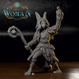Unpainted grey resin physical print of Bonnie the Harengon Druid miniature on a wooden surface — front view showing the printed detail of her flame-raised fist, staff, feathered armour, braided hair, and rabbit ears
