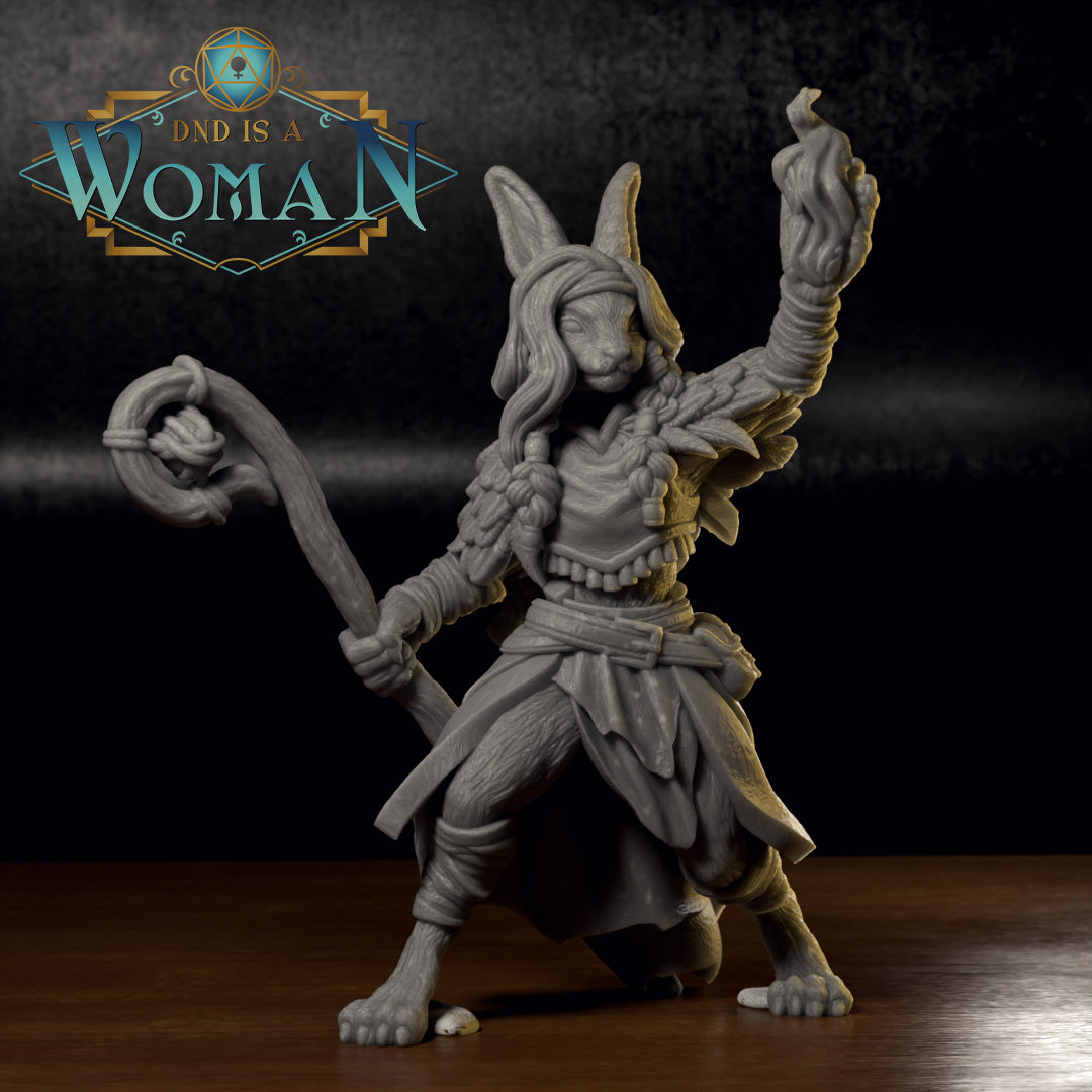 Unpainted grey resin physical print of Bonnie the Harengon Druid miniature on a wooden surface — front view showing the printed detail of her flame-raised fist, staff, feathered armour, braided hair, and rabbit ears