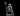 Chubby raccoon druid standing upright, gripping a tall curved staff in one clawed hand, other hand raised with splayed claws. Wears a hooded cloak clasped at chest and a belted satchel. Gaze tilted upward. Sculpt by MZ4250.
