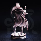 Unpainted grey resin miniature of Ridan the Everlasting — rear view showing the intricate texture of the billowing tattered cloak, chainmail back plate, and spiked crown. Photographed on a dark background.