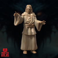 Robed male human figure with both arms raised — one hand pointing two fingers upward, one hand outstretched with splayed fingers. Long hair, star amulet at chest, layered cowl and floor-length robes, sandalled feet. Sculpt by Monster Atlas.