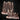 Digital render of two rustic wooden fence terrain pieces by Mia Kay M3DM — a large five-stake palisade section and a small two-stake broken section, both with rope bindings and scrubby ground detail, shown in warm grey resin tones against a dark background