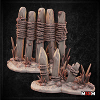 Digital render of two rustic wooden fence terrain pieces by Mia Kay M3DM — a large five-stake palisade section and a small two-stake broken section, both with rope bindings and scrubby ground detail, shown in warm grey resin tones against a dark background