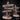 Digital render of two rustic wooden signpost terrain pieces by Mia Kay M3DM. The larger post has four rope-bound planks carved with glyphs and numerals pointing in multiple directions; the smaller has three boards. Both sit on oval bases with desert scrub grass and bulbous plants. Unpainted resin colourway.
