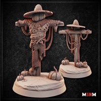 Scarecrow miniature shown at close range, pumpkin head and straw hat visible above the woven wicker torso, rope-bound crossbeam arms, decorative base with scattered pumpkins at the foot of the post. Sculpt by Mia Kay M3DM.