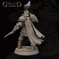 Rear view of the same unpainted grey resin Queen's Guard Sergeant miniature showing the full sweep of the dramatic flowing cape, detailed segmented armour on the back and shoulders, plumed helmet, and the longsword extended outward from the lowered left arm, set on a cracked cobblestone scenic base