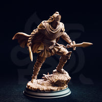 Front view of an unpainted resin miniature of a dark cultist warrior in layered armour with a sun-eye visor helm, dual blades drawn, billowing cloak, and geometric-patterned pauldrons, mounted on a detailed rocky scenic base