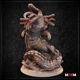 Sewer Serpent miniature by Mia Kay M3DM shown beside a D20 die for scale reference, multi-headed body with open jaws and clawed limbs, mounted on a cracked-ground decorative base in grey unpainted resin.
