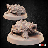 Digital render of two Snapping Turtle miniatures by Mia Kay M3DM — one showing the spiked shell from above with head partially retracted, the other with neck extended and beak-like jaws wide open, both on oval bases