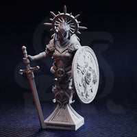 Photograph of unpainted grey resin Soleria the Judge bust miniature — front view showing detailed plate armour with sacred engravings, spiked wheel halo, round shield with intricate scrollwork and central winged figure, and cruciform sword, on an ornate stepped display base