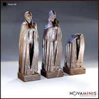 Three robed humanoid statues on square stone bases showing progressive ruin: left figure intact with deep cloak folds, centre figure cracked open, right figure broken at the torso. Sculpt by Novaminis.