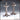 Two tall iron candelabras by Novaminis: left has a square four-arm crown with single central socket; right has a clustered six-socket multi-tiered crown. Both stand on bolted tripod bases with splayed feet.