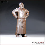 Heavyset bald barman standing with both hands on hips, wearing a long apron with a twisted rope tie at the waist, short beard, and a tunic clasped at the collar. Sculpt by Novaminis.