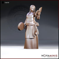 Female cook holding an open book raised in her right hand and gripping a flat pan under her left arm, wearing a laced bodice, layered skirts, and a rope belt with a ladle and pouch. Sculpt by Novaminis.