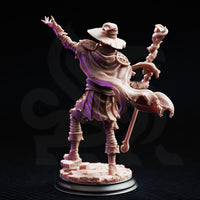 Rear three-quarter view of the same Dragonblight Stricken Student miniature — unpainted resin showing the detailed back of tattered robes with scale-like texture, the wide witch-style hat, and the corrupted staff with flame and curved talon detail, on a rubble base