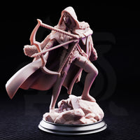Female hooded archer with crossbow at full draw, cloaked figure in leather armour with fur-trimmed shoulders, calm focused expression partially shadowed by deep hood, on a rocky scenic base. Sculpt by DM Stash.
