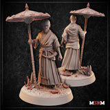 Umbrella Spear Monk shown at tabletop beside a large d20 die — shaven-headed figure in belted robes holding an umbrella-tipped spear, bare feet, narrow goatee, serene expression. Sculpt by Mia Kay M3DM.