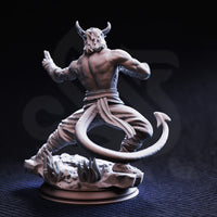 Rear view of the unpainted grey resin Verek Heartless tiefling monk miniature, showing the sweep of his long barbed tail, defined back musculature, rope-wrapped legs, and the stone spike base with a circular plinth beneath