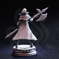 Rear three-quarter photograph of unpainted grey resin Vika 'Doll Lips' miniature — showing the full sweep of her long coat, back armour detail, and the engraved blades of the halberd raised overhead, on an ornate round display base