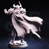Photograph of Vilnais the Ashen unpainted grey resin miniature from behind — showcasing the extraordinary texture detail of the woven fabric cape sweeping to one side, both arms outstretched, spiked pauldrons visible over the shoulders.