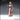 Front view of the Creepy Human Child 01 miniature — an unpainted resin render of a young girl in a long plain dress, one arm raised with a single finger pointing outward, holding a worn ragdoll in her other hand, with a long braid over her shoulder. Novaminis branding visible.