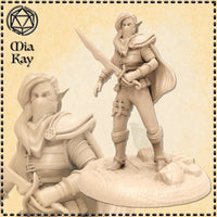 Unpainted resin miniature of a masked female elf rogue at 32mm scale, standing on a rocky scenic base with longsword raised and cloak billowing behind her — sculpted by Mia Kay M3DM
