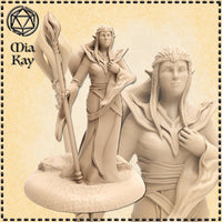 Unpainted resin render of a female elf sorceress miniature at 32mm scale, holding a tall leaf-tipped wooden staff in her left hand with her right hand resting on her chest. She wears layered flowing robes with a wide collar, and her long hair is styled in braided rows. The base is detailed with scattered rocks. A close-up inset shows the expressive face and braided hairstyle in fine detail. Sculpted by Mia Kay M3DM.